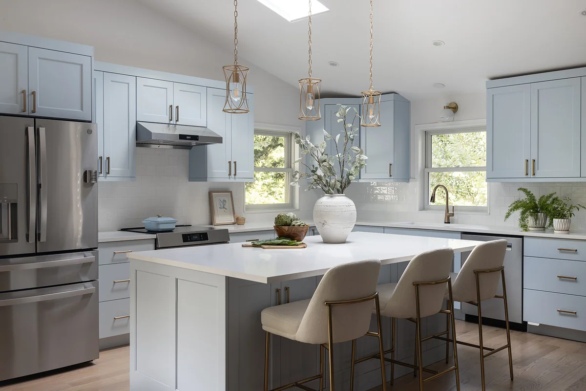 Pale-blue kitchen with a white stone island, L-shaped countertops and a white tile backsplash.