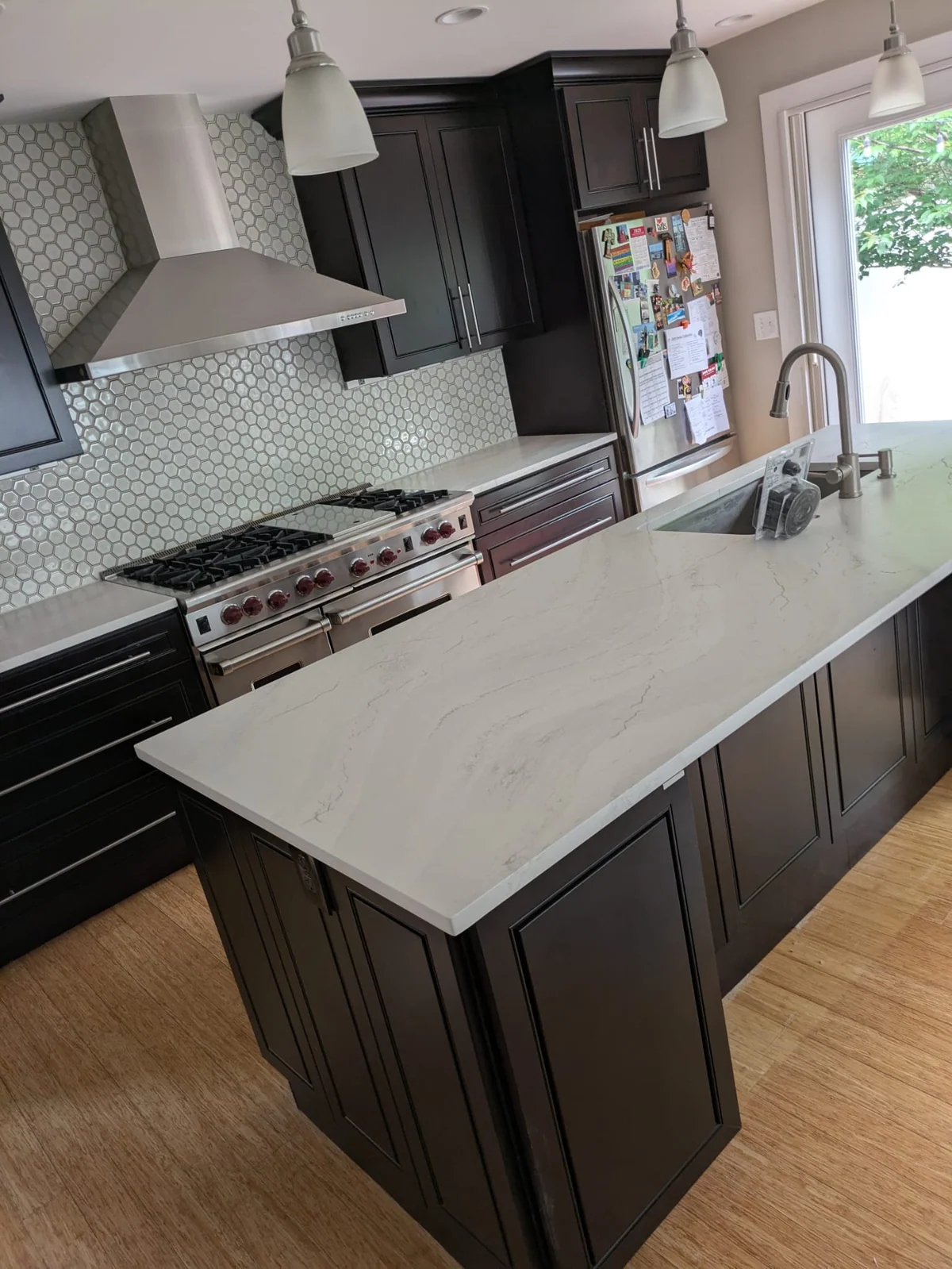 Light stone island with a sink, dark kitchen cabinetry and a hexagonal tile backsplash.