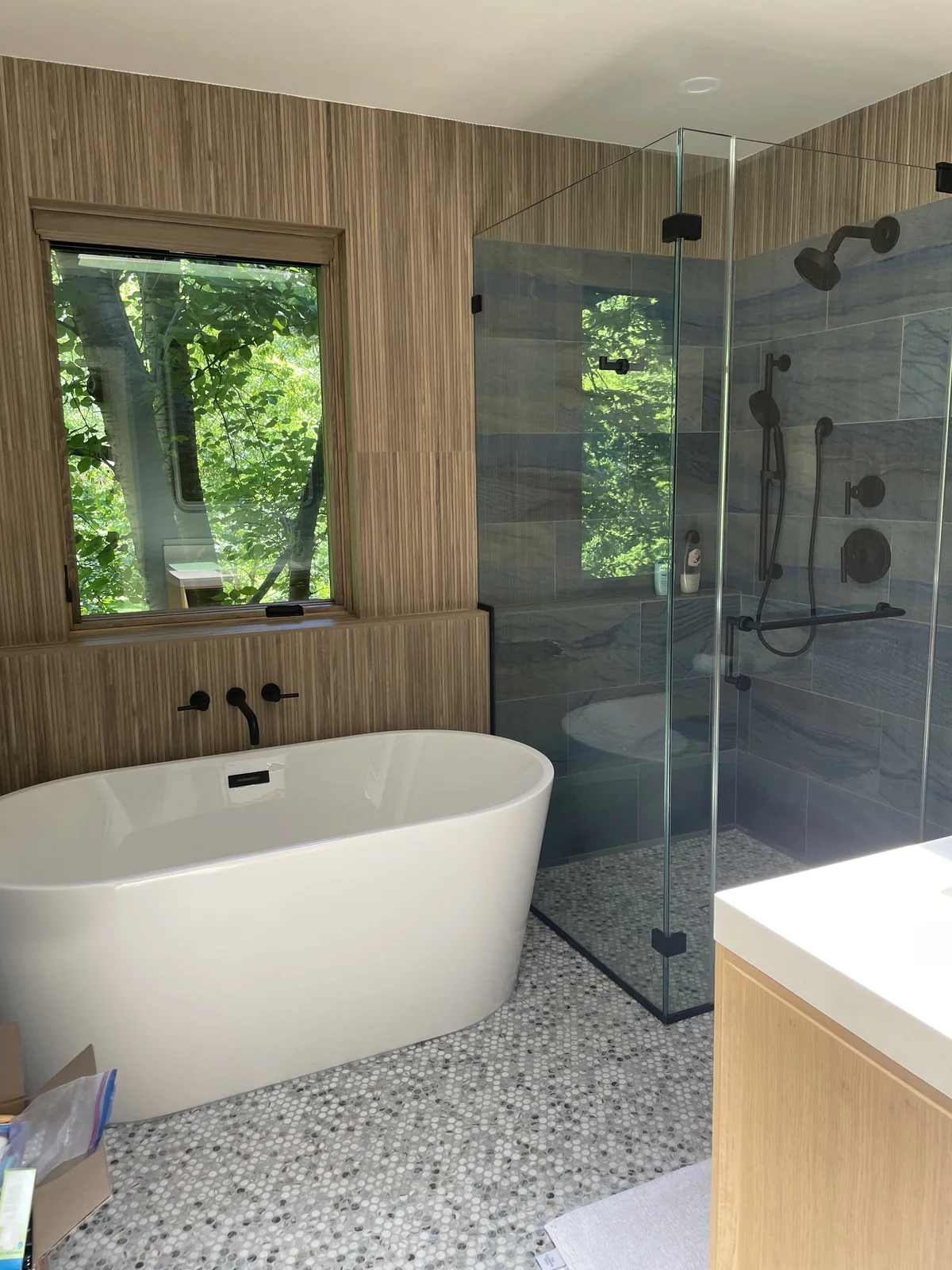 Bathroom with wood-look wall tile, a porcelain shower and natural-stone flooring beside a freestanding tub.