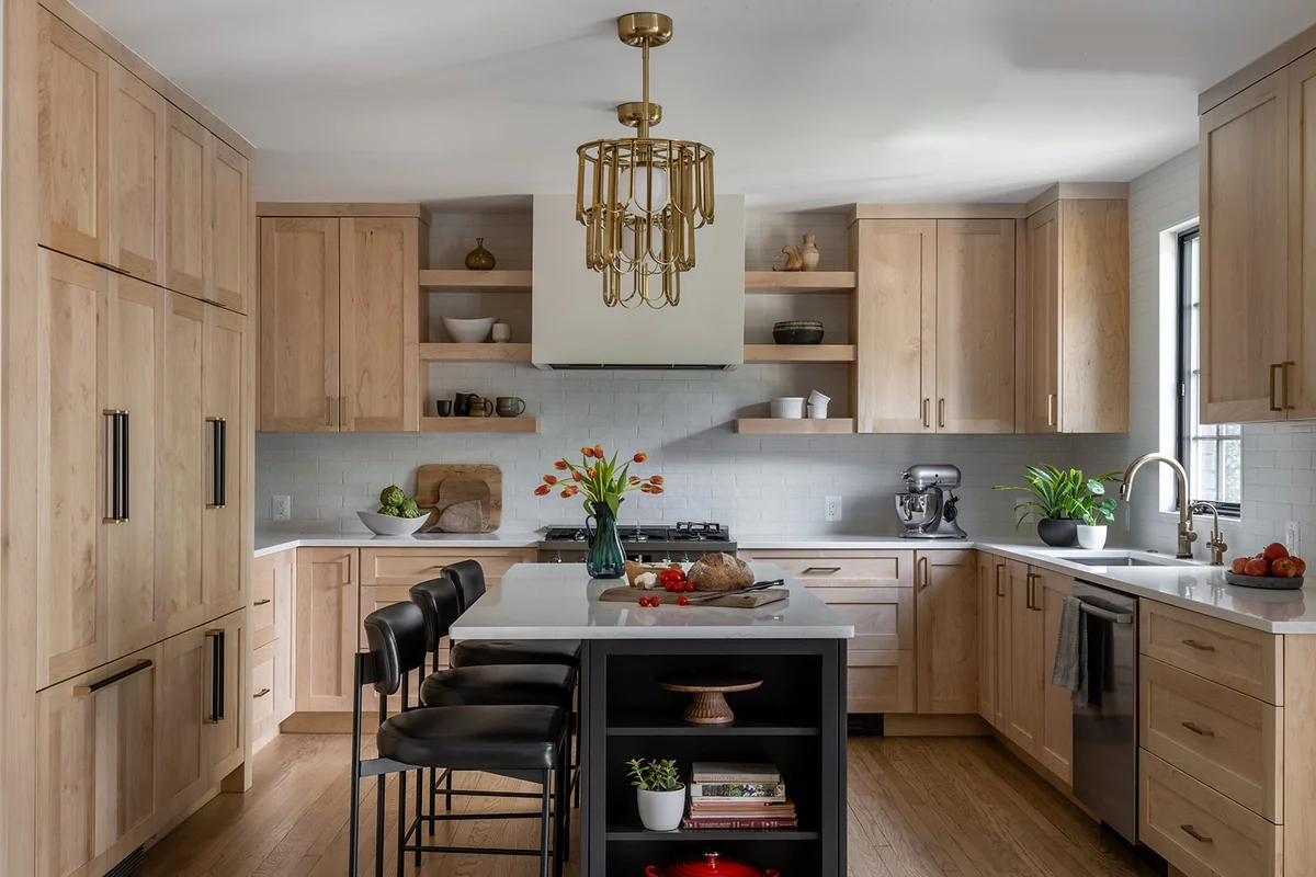 Kitchen with natural wood cabinetry, a dark island, pale stone surfaces and a light backsplash.