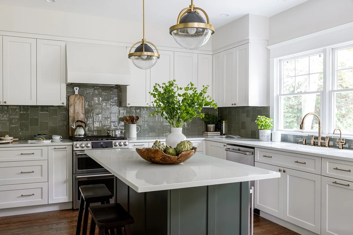 White kitchen with a dark custom island, light countertops and a green artisan tile backsplash.