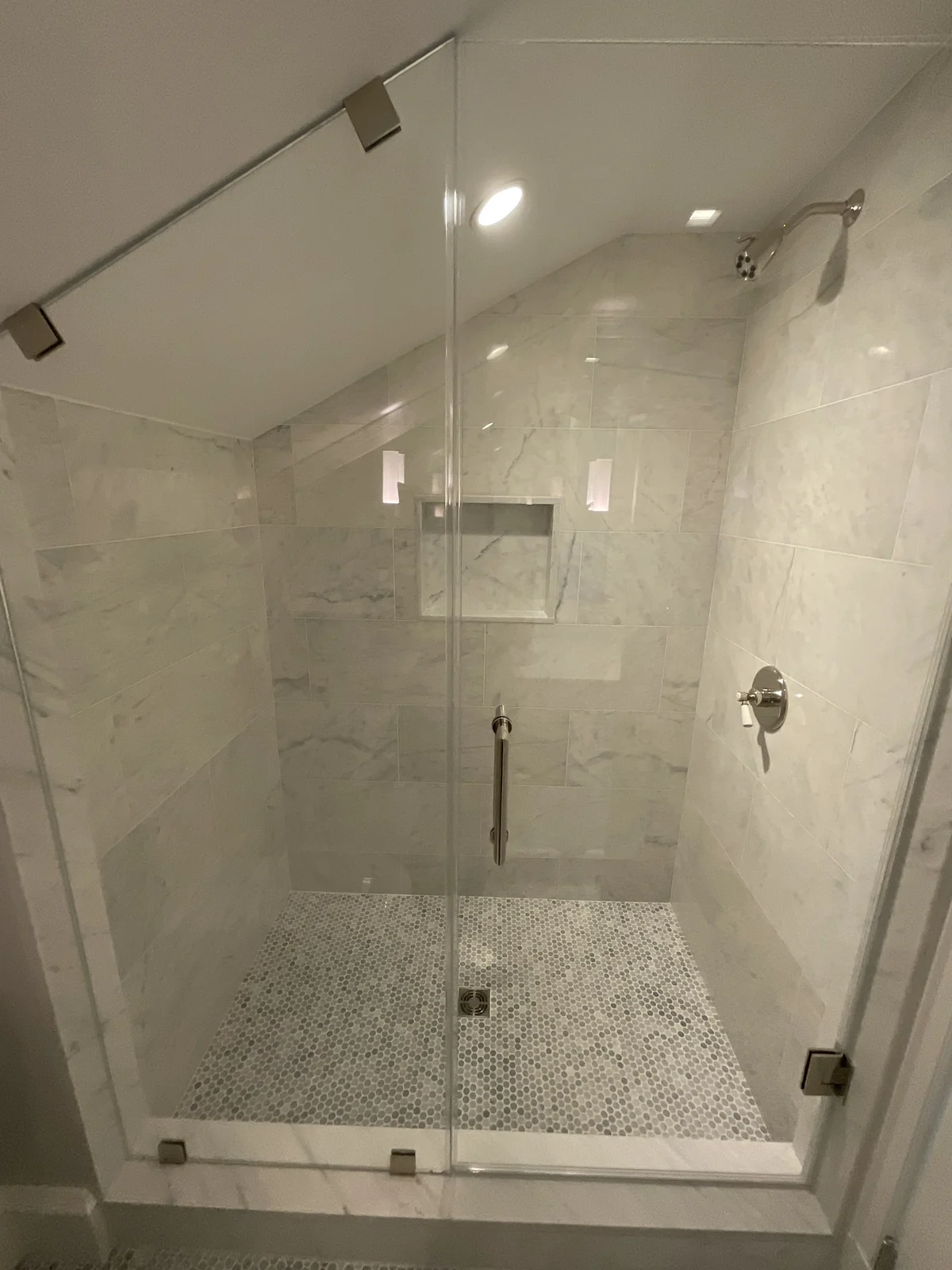 Finished shower with pale wall tile, recessed niche, glass enclosure and small mosaic floor tiles