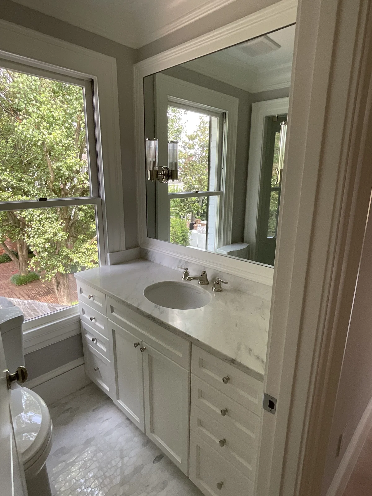 White bathroom vanity with stone countertop, oval sink and a window overlooking trees